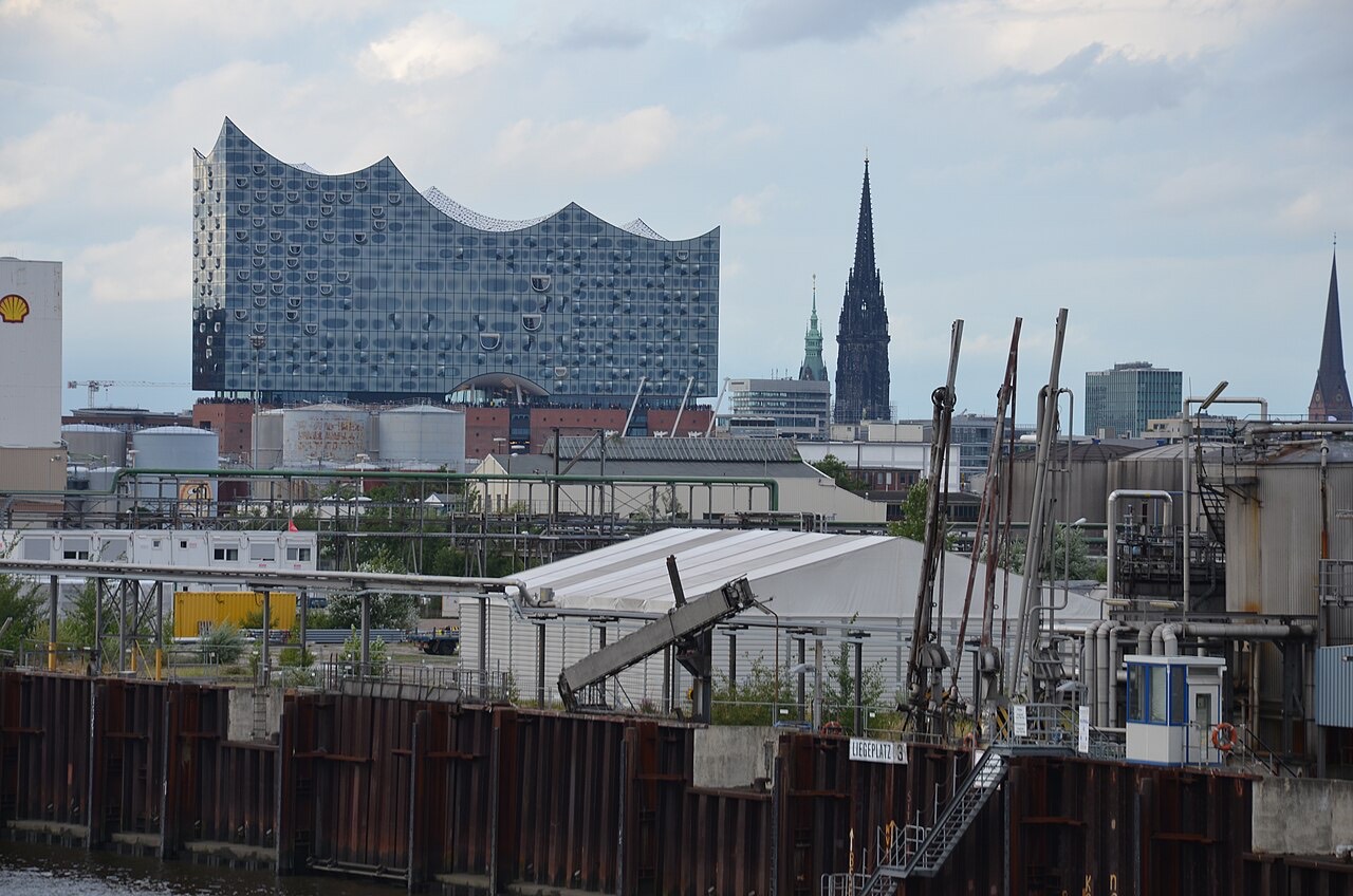 Die Elbphilharmonie in Hamburg mit ihrer wellenförmigen Glasfassade auf dem historischen Backsteinsockel, im Vordergrund das Wasser der Elbe
